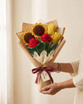 Wrapped crochet bouquet of roses, sunflowers and tulips held in two hands