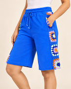 Close view of cobalt Bermuda shorts showing crocheted granny squares framing the pocket
